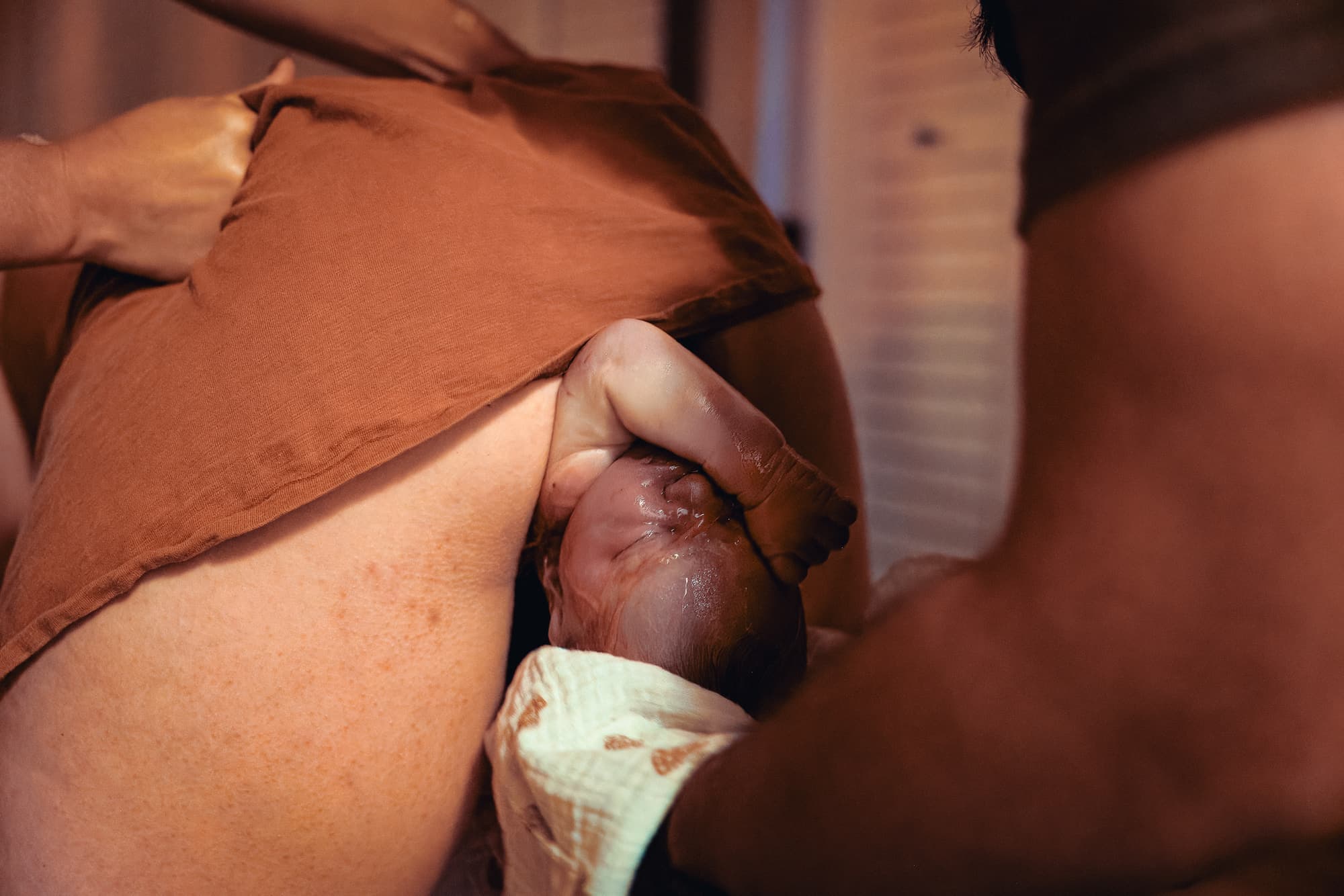 A just-born baby lifted to the mother's chest in warm home light