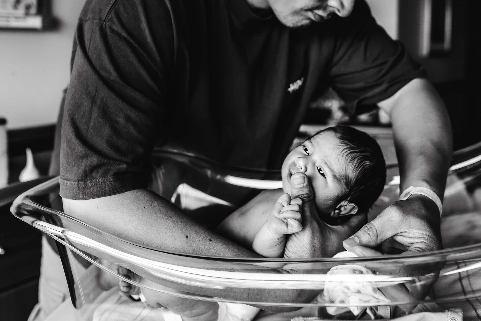 A father leaning over the bassinet as his newborn brings a hand to its mouth