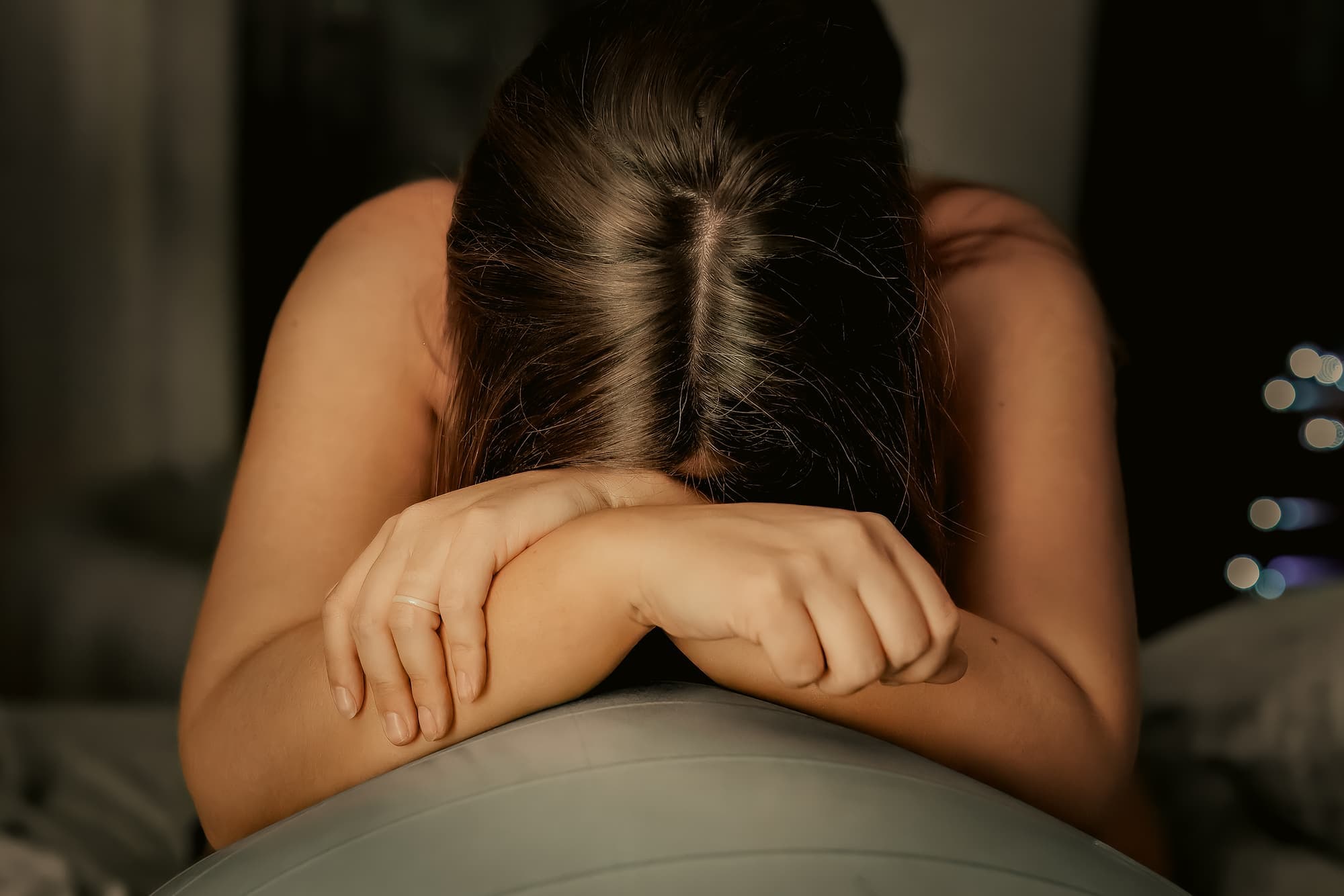 A laboring mother resting her head on crossed arms over a birth ball
