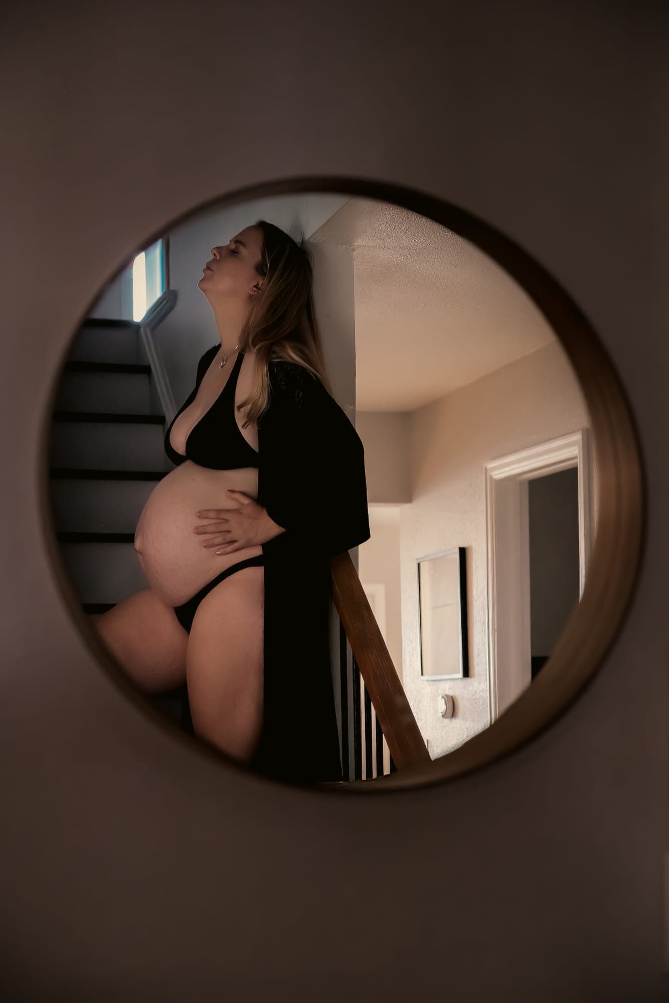 A pregnant mother leaning against the stairwell wall, reflected in a round mirror