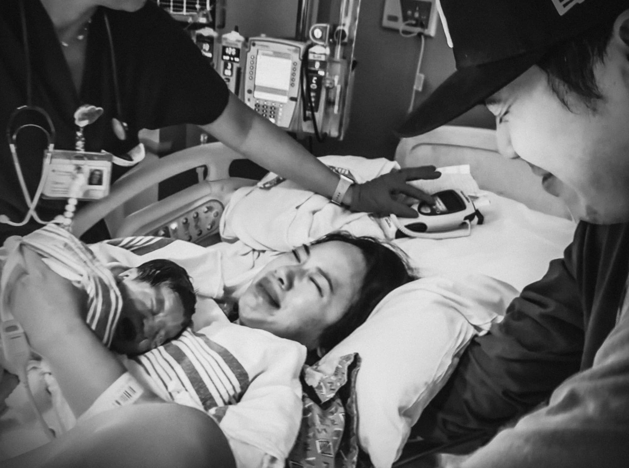 A mother resting with her newborn as a support person strokes her head