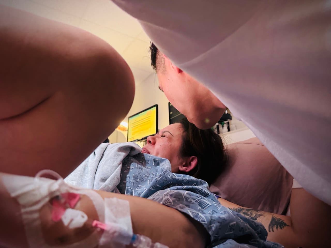 A low view of a mother bearing down in a hospital bed as her partner leans in close