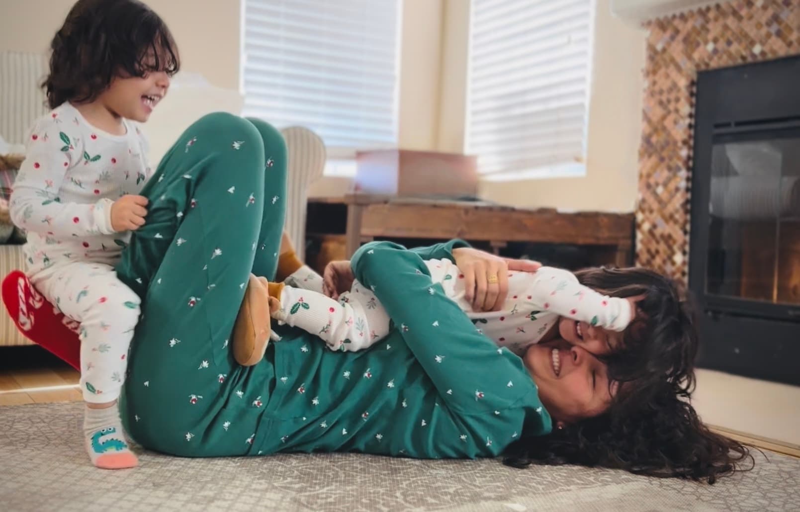 Maribel laughing on the floor as she plays with her toddler by the fireplace