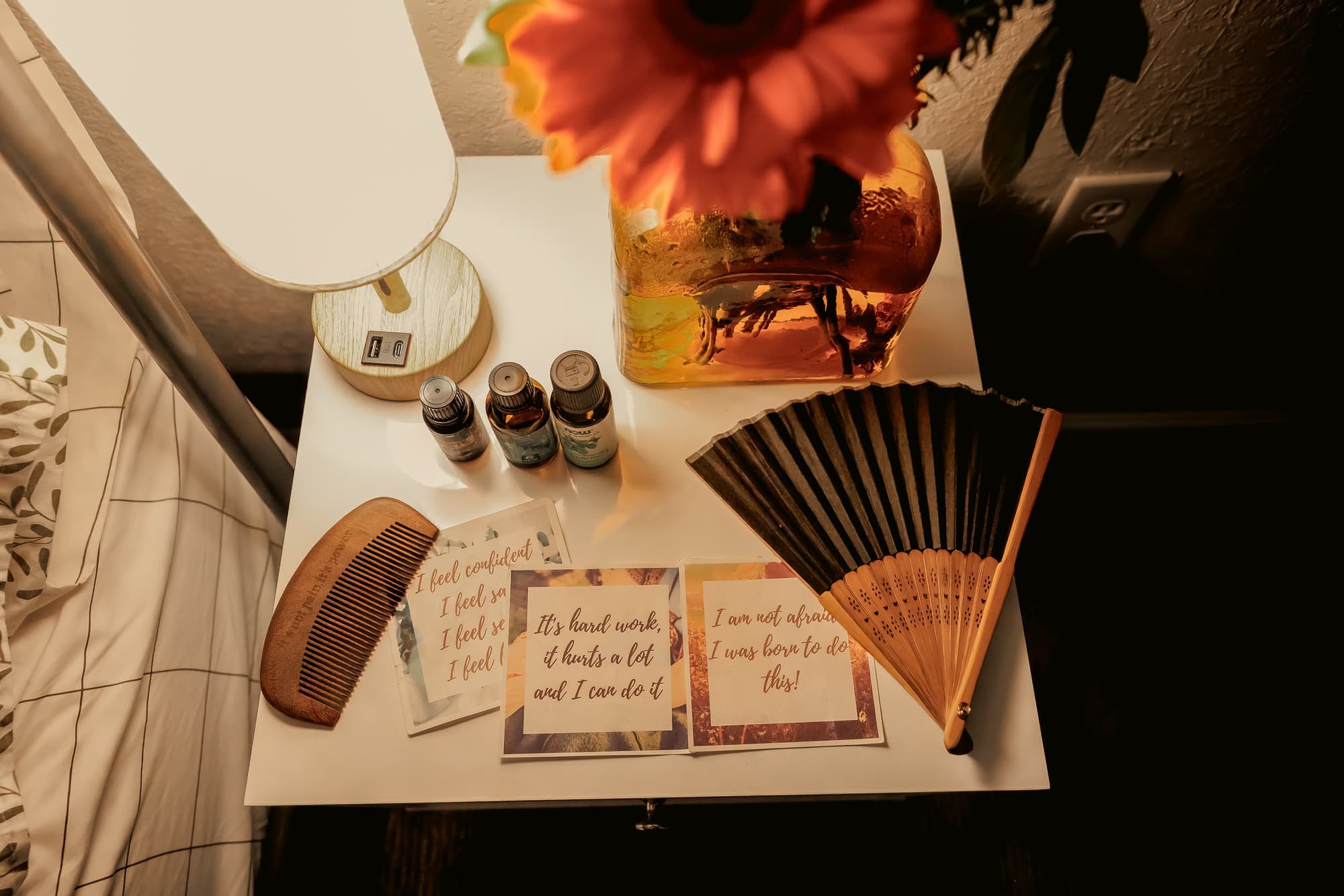 A bedside comfort toolkit with essential oils, a wooden comb, a folding fan, and printed birth affirmation cards