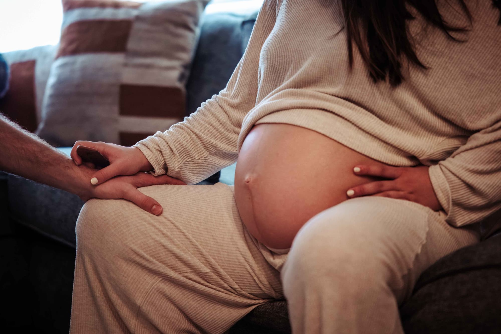 An expectant mother resting a hand on her belly while holding her partner's hand