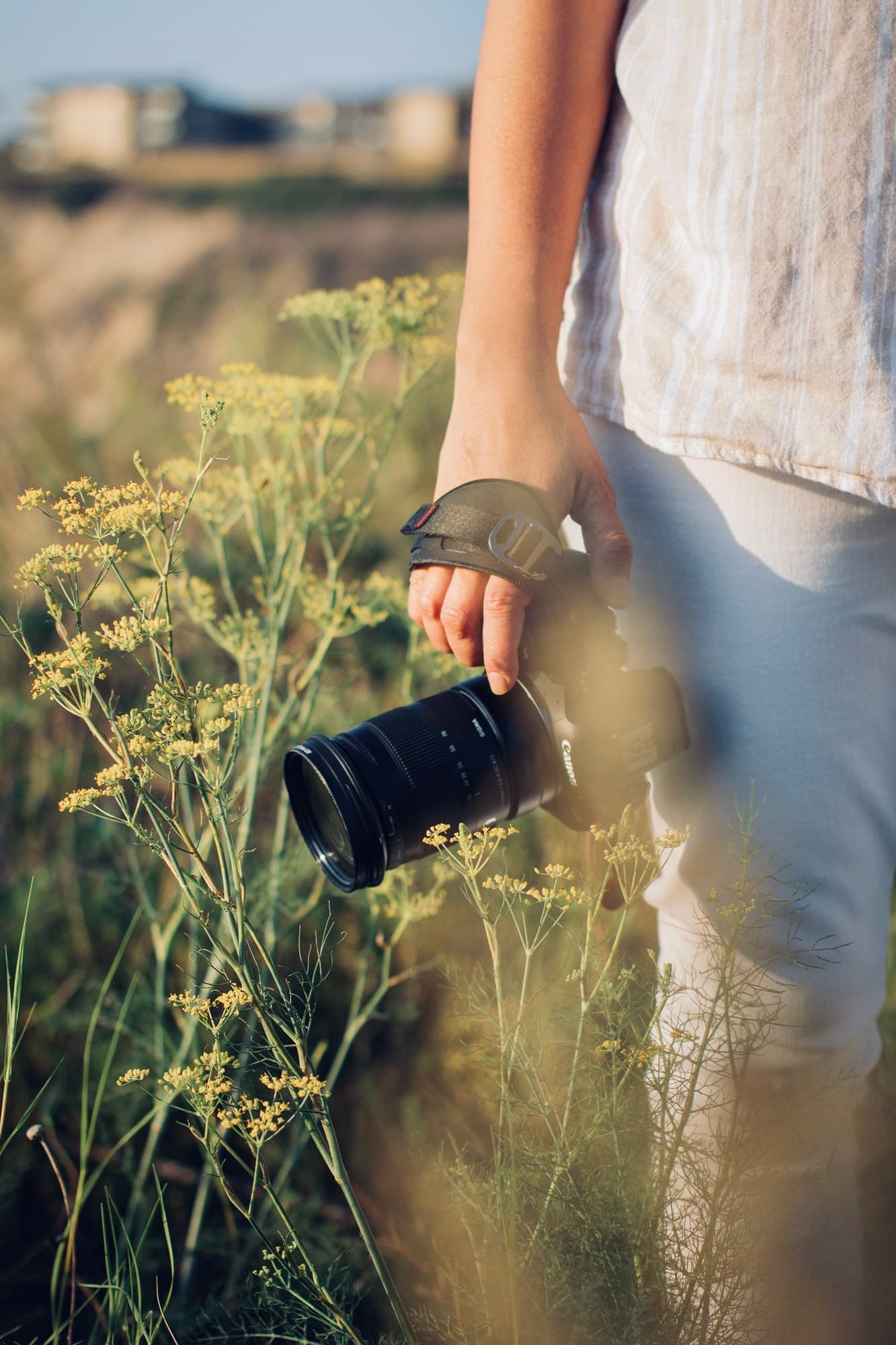 Maribel walking through a sunlit field of wildflowers with her camera in hand, coastal Orange County hills behind her