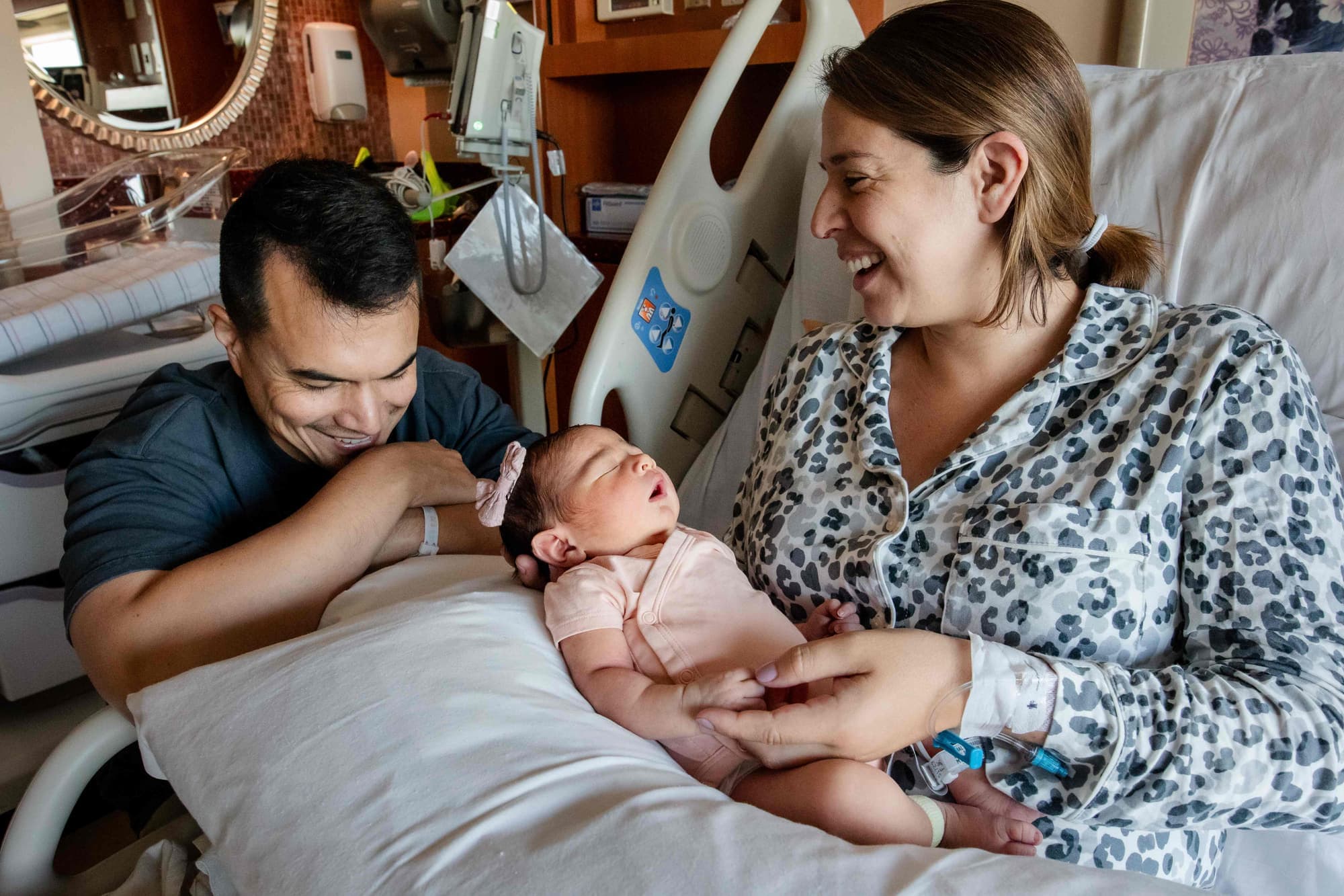 New parents smiling down at their newborn resting in a hospital bed just after birth