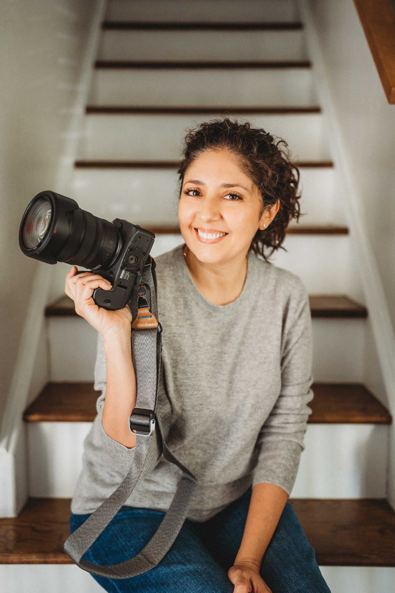 Maribel seated on a staircase, smiling and holding her camera