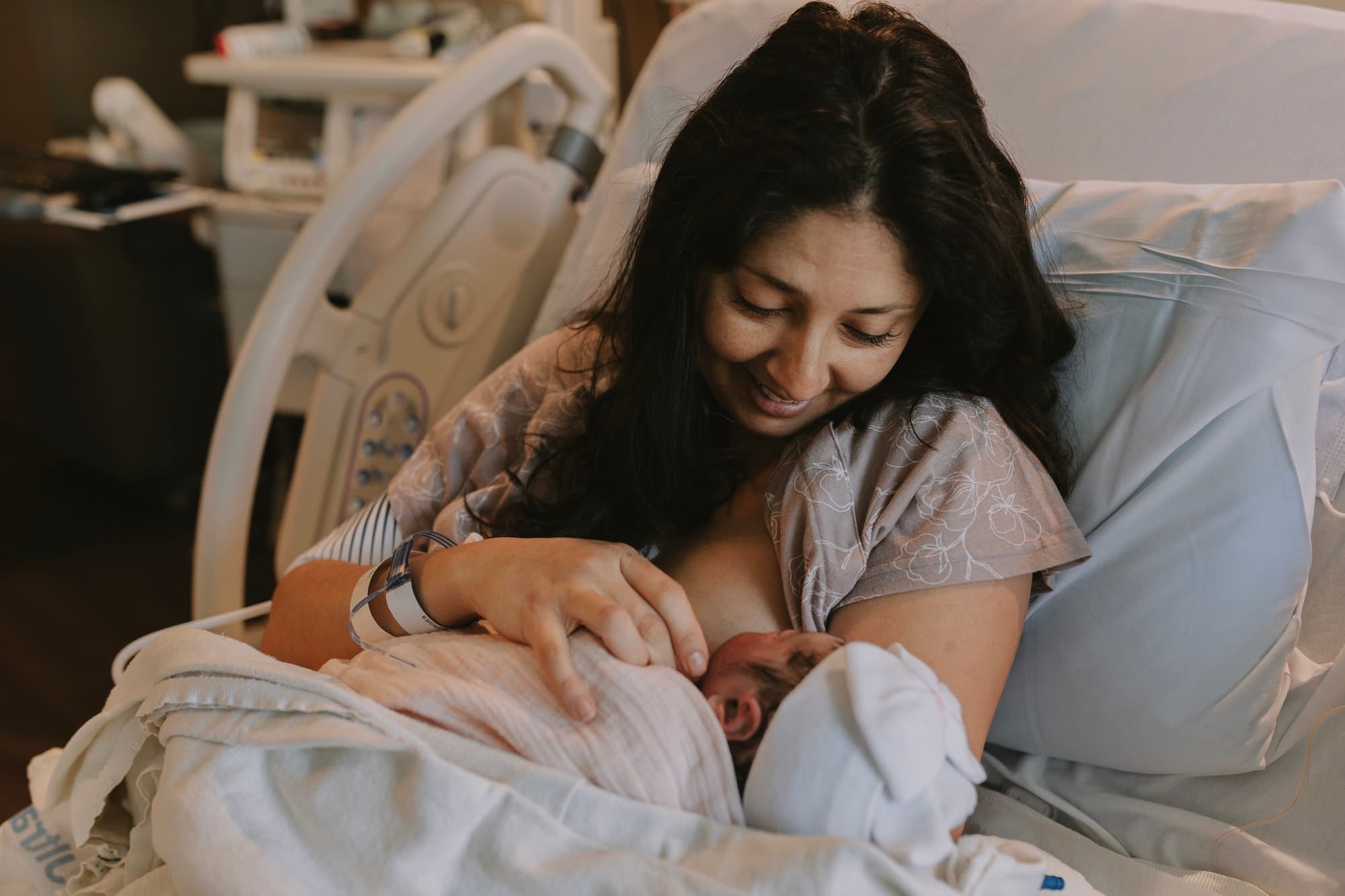 A mother smiling down at her newborn as they nurse skin-to-skin in the hospital just after birth